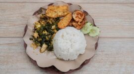 Sepiring nasi kuning pulen disajikan dengan lauk-pauk komplit seperti ayam goreng, telur balado, sambal goreng kentang, dan irisan timun segar, menggambarkan kelezatan serta kekayaan kuliner Nusantara. Hidangan ini memancarkan warna kuning cerah yang menggoda selera, siap memanjakan setiap penikmatnya.