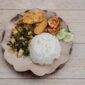 Sepiring nasi kuning pulen disajikan dengan lauk-pauk komplit seperti ayam goreng, telur balado, sambal goreng kentang, dan irisan timun segar, menggambarkan kelezatan serta kekayaan kuliner Nusantara. Hidangan ini memancarkan warna kuning cerah yang menggoda selera, siap memanjakan setiap penikmatnya.