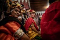 Seorang balian atau dukun adat Dayak Benuaq sedang melakukan ritual Belian, menari dalam kondisi trans diiringi musik tradisional, memohon kesembuhan dan keseimbangan alam. Pakaian adat dan ornamen khas menambah kesan sakral pada upacara yang sarat makna spiritual ini.