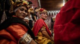 Seorang balian atau dukun adat Dayak Benuaq sedang melakukan ritual Belian, menari dalam kondisi trans diiringi musik tradisional, memohon kesembuhan dan keseimbangan alam. Pakaian adat dan ornamen khas menambah kesan sakral pada upacara yang sarat makna spiritual ini.