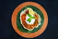 Sajian tumpeng nasi kuning yang ikonik dengan aneka lauk pauk tradisional, melambangkan syukur dan kemakmuran dalam berbagai perayaan di Indonesia. Hidangan ini memancarkan kehangatan dan kekayaan budaya kuliner Nusantara.