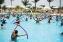 Sekelompok wanita lanjut usia tersenyum ceria saat melakukan gerakan aqua aerobik di dalam kolam renang, menunjukkan betapa olahraga air dapat dinikmati oleh semua kalangan usia. Air memberikan dukungan yang lembut sehingga latihan kebugaran terasa lebih ringan dan menyenangkan.