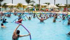 Sekelompok wanita lanjut usia tersenyum ceria saat melakukan gerakan aqua aerobik di dalam kolam renang, menunjukkan betapa olahraga air dapat dinikmati oleh semua kalangan usia. Air memberikan dukungan yang lembut sehingga latihan kebugaran terasa lebih ringan dan menyenangkan.