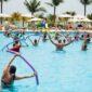 Sekelompok wanita lanjut usia tersenyum ceria saat melakukan gerakan aqua aerobik di dalam kolam renang, menunjukkan betapa olahraga air dapat dinikmati oleh semua kalangan usia. Air memberikan dukungan yang lembut sehingga latihan kebugaran terasa lebih ringan dan menyenangkan.