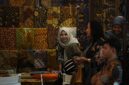 Seorang perajin batik dari Kalimantan Timur sedang dengan teliti menyelesaikan proses pewarnaan pada sehelai kain, menampilkan motif-motif khas flora dan fauna Borneo yang kaya akan detail dan makna.