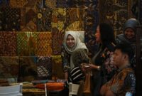 Seorang perajin batik dari Kalimantan Timur sedang dengan teliti menyelesaikan proses pewarnaan pada sehelai kain, menampilkan motif-motif khas flora dan fauna Borneo yang kaya akan detail dan makna.