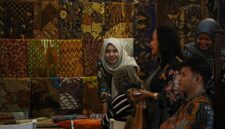 Seorang perajin batik dari Kalimantan Timur sedang dengan teliti menyelesaikan proses pewarnaan pada sehelai kain, menampilkan motif-motif khas flora dan fauna Borneo yang kaya akan detail dan makna.