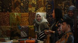 Seorang perajin batik dari Kalimantan Timur sedang dengan teliti menyelesaikan proses pewarnaan pada sehelai kain, menampilkan motif-motif khas flora dan fauna Borneo yang kaya akan detail dan makna.