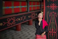 Seorang model berpose anggun mengenakan gaun bermotif batik khas Kalimantan Timur, menampilkan perpaduan harmonis antara desain modern dan kekayaan budaya lokal. Gaun ini menonjolkan motif anggrek hitam dan burung enggang yang elegan, mencerminkan keindahan alam Borneo.