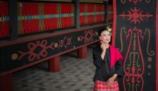 Seorang model berpose anggun mengenakan gaun bermotif batik khas Kalimantan Timur, menampilkan perpaduan harmonis antara desain modern dan kekayaan budaya lokal. Gaun ini menonjolkan motif anggrek hitam dan burung enggang yang elegan, mencerminkan keindahan alam Borneo.