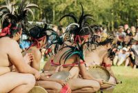 Seorang Balian, pemimpin ritual Belian dari suku Dayak Benuaq, mengenakan pakaian adat lengkap saat memimpin upacara sakral di tengah hutan Kalimantan. Kostumnya yang kaya detail dan penuh makna, dihiasi manik-manik serta bulu burung, melambangkan koneksi mendalam dengan alam dan roh leluhur.