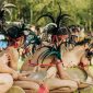 Seorang Balian, pemimpin ritual Belian dari suku Dayak Benuaq, mengenakan pakaian adat lengkap saat memimpin upacara sakral di tengah hutan Kalimantan. Kostumnya yang kaya detail dan penuh makna, dihiasi manik-manik serta bulu burung, melambangkan koneksi mendalam dengan alam dan roh leluhur.
